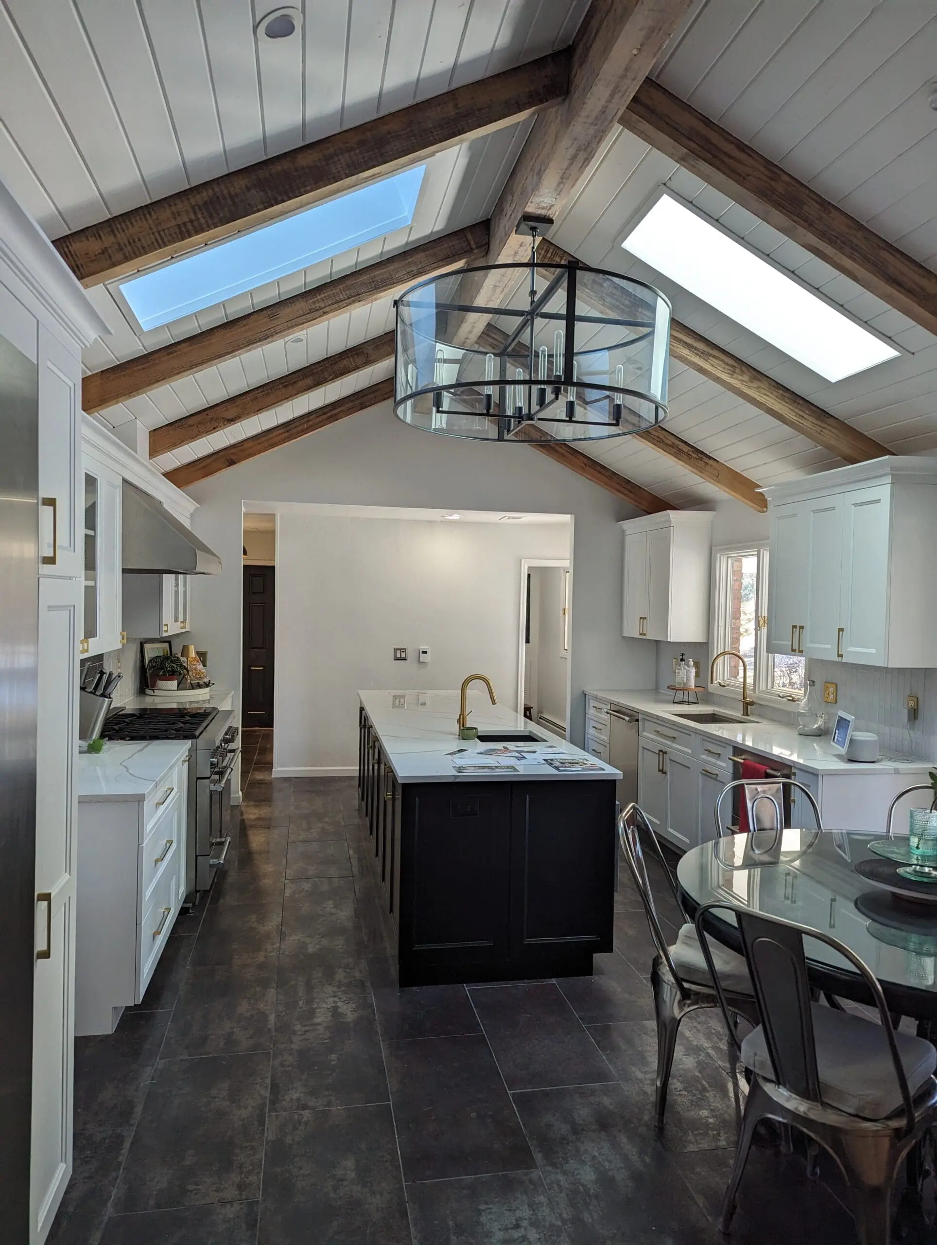 Professional interior residential remodeling featuring a modern white kitchen with custom cabinets, an oversized dark island, and exposed wood ceiling beams.