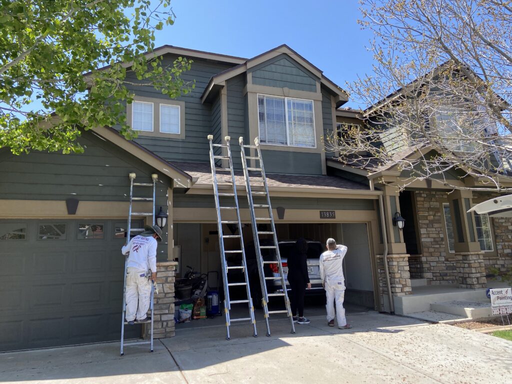 Exterior of home with paint crew on ladders working and talking with homeowner