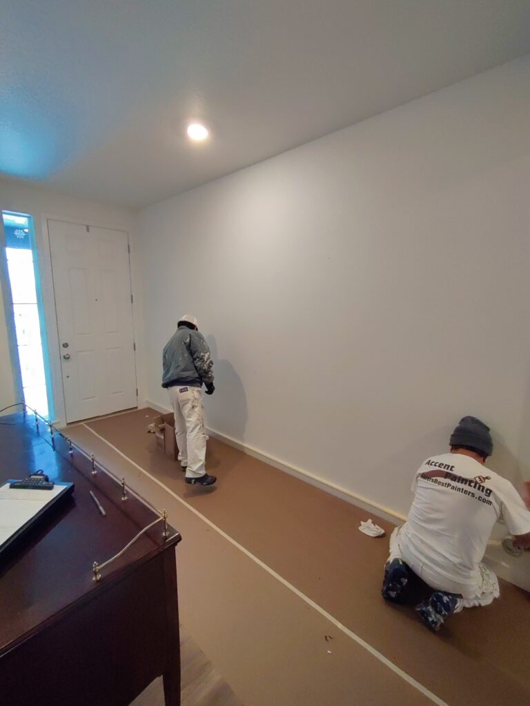 Two painters masking baseboard of home for painting