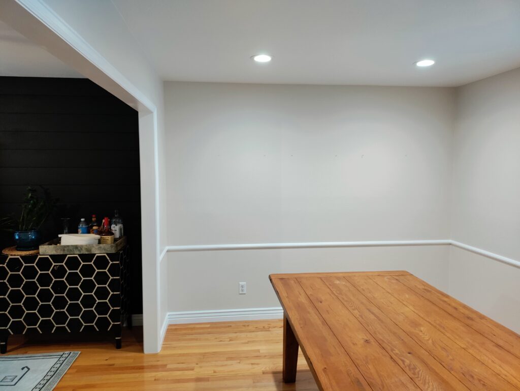 Natural wood kitchen table in white dining room next to small bar