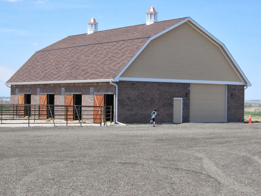 Wide view of a large commercial barn with gambrel roof and light tan paint and brick