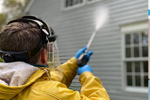 Closeup of person power washing house siding