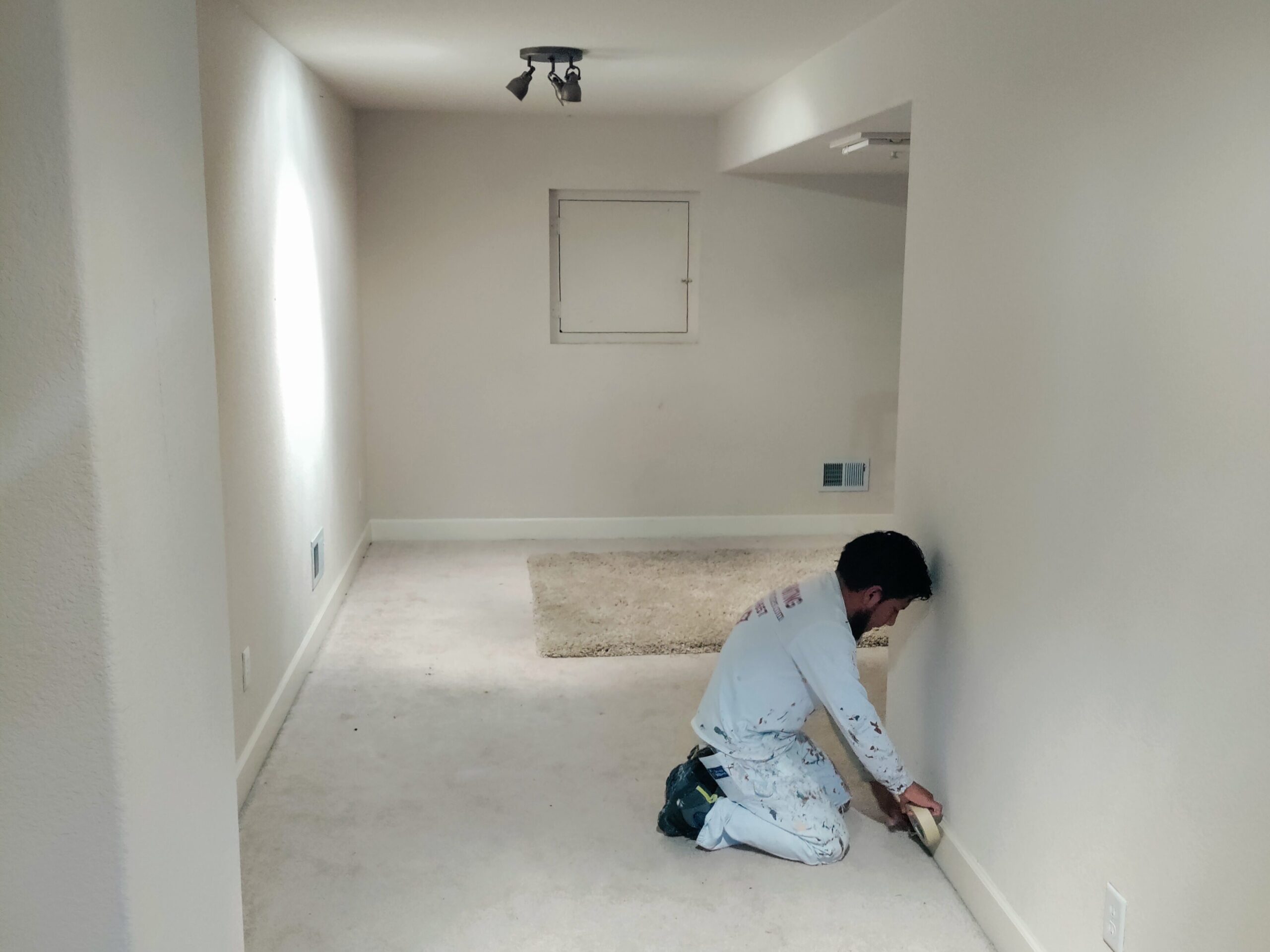 Worker taping baseboards for painting