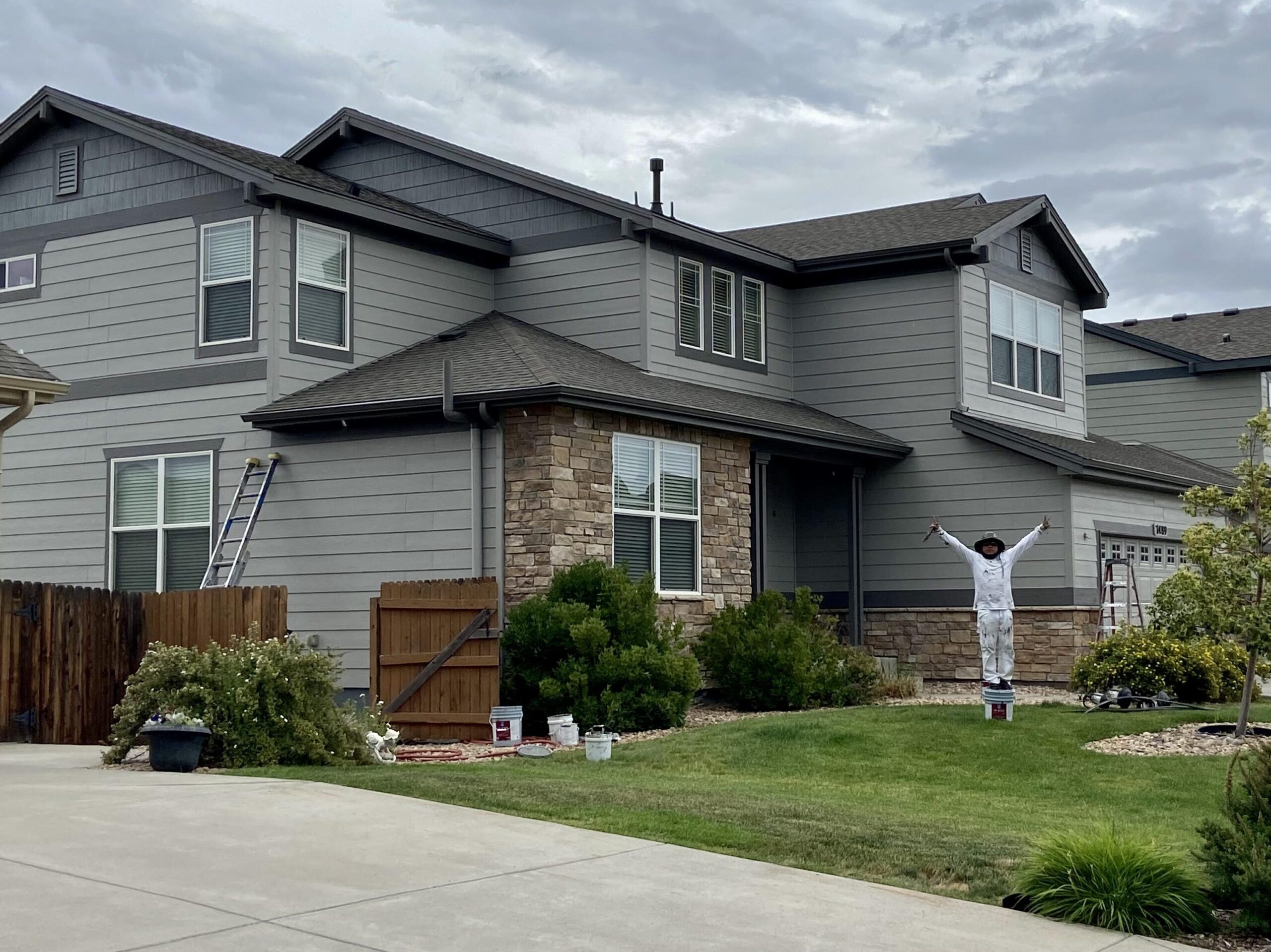 Wide angle view of man raising arms in front of home painted with tan siding and dark grey trim